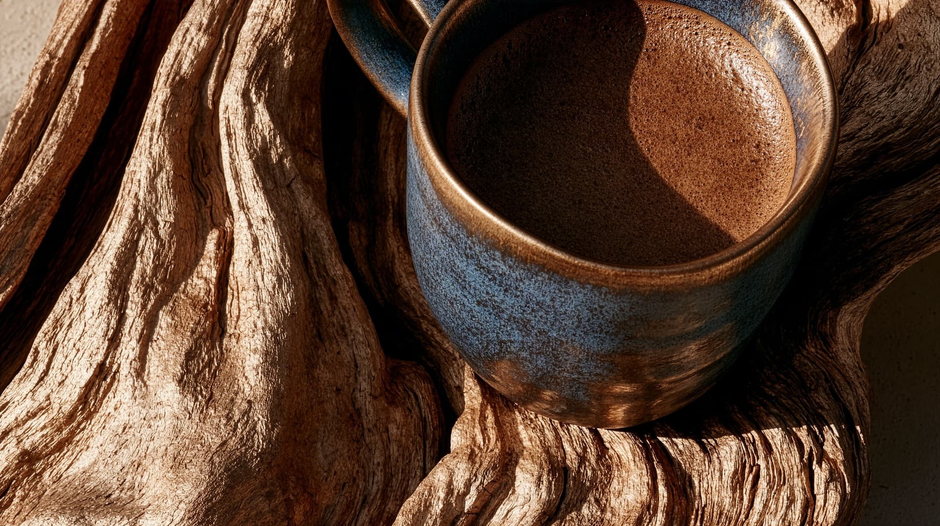 A blue-glazed cup of brewed mesquite resting on bark